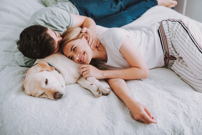 Kuschelndes Paar liegt mit Hund im Bett