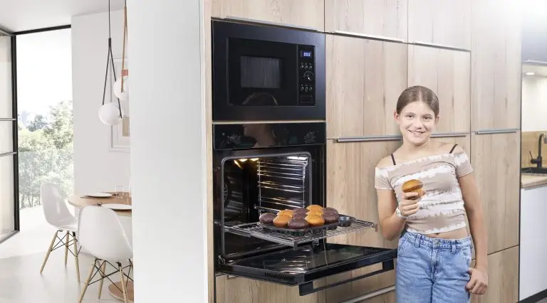 Ein Mädchen steht vor einem ORANIER EBS220-Einbaubackofen und holt einen Muffin aus dem Backofen und über dem Backofen ist eine ORANIER HMG360-Mikrowelle.