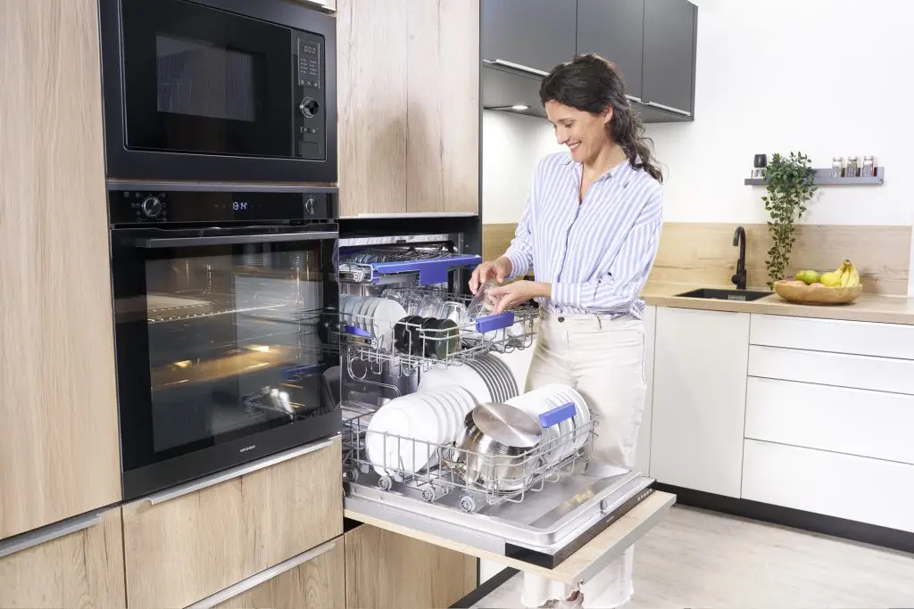 Eine junge Frau, die neben einem ORANIER GSV660-Geschirrspüler steht, und neben ihr steht ein ORANIER EBS420-Backofen und über dem Backofen eine ORANIER HMG360-Mikrowelle.