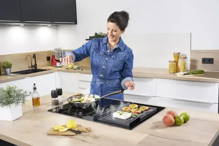 Eine junge Frau, die in einer modernen Küche auf der Kochinsel kochen, mit einem ORANIER KFA590-Kochfeldabzug und mit einer Grillplatte von ORANIER KGP260.