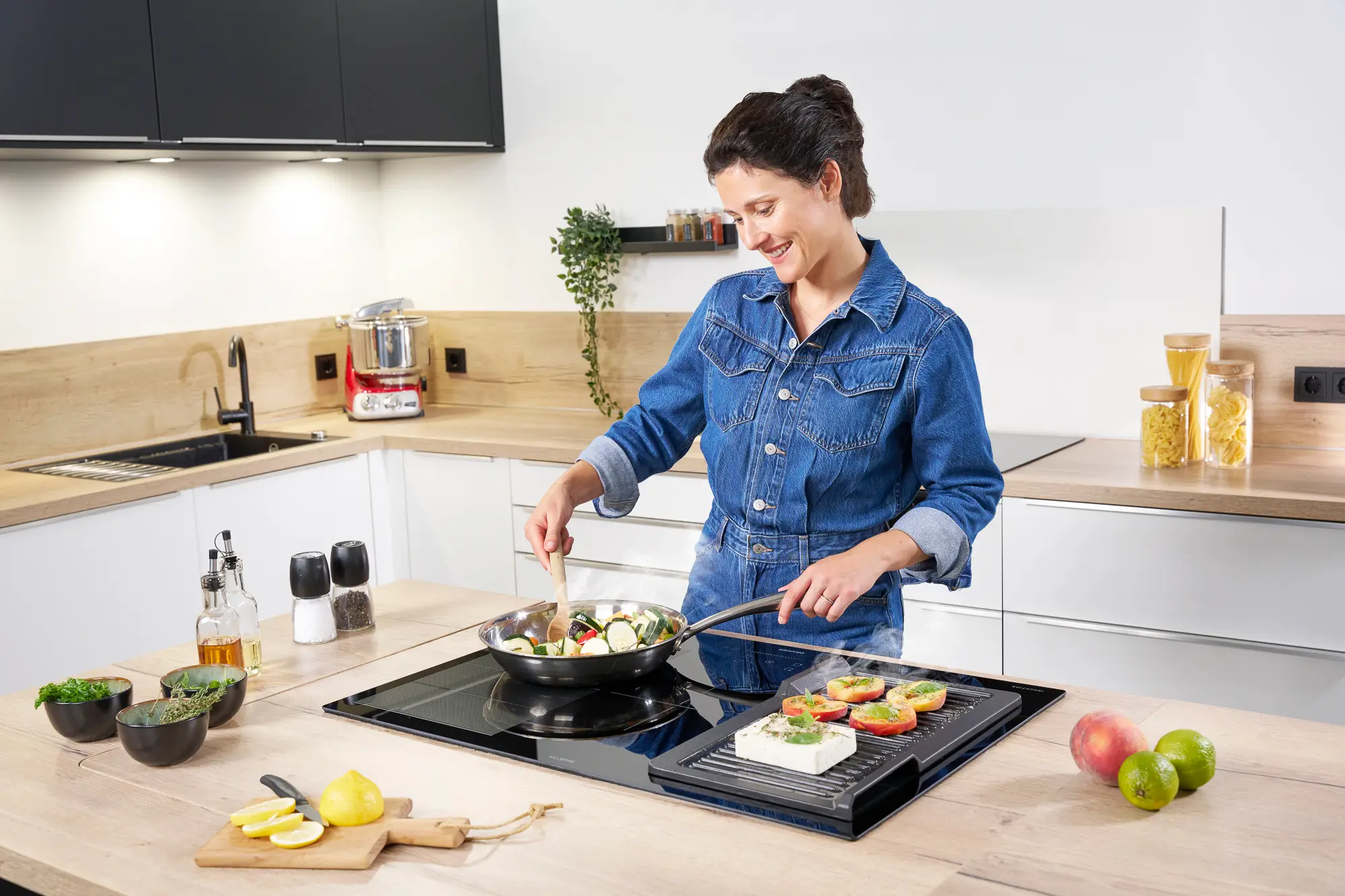 Eine junge Frau, die in einer modernen Küche auf der Kochinsel kochen, mit einem ORANIER KFA590-Kochfeldabzug und mit einer Grillplatte von ORANIER KGP260.