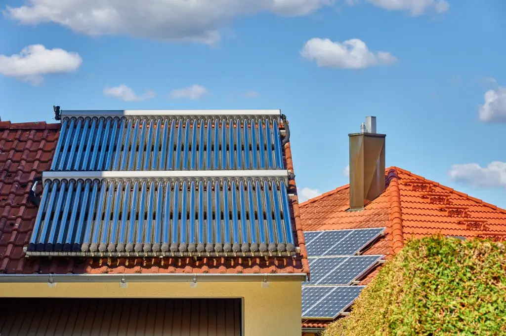Solarthermieanlage auf dem Dach eines Hauses. Im Hintergrund eine Photovoltaikanlage.