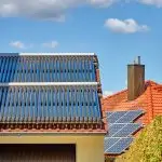 Solarthermieanlage auf dem Dach eines Hauses. Im Hintergrund eine Photovoltaikanlage.