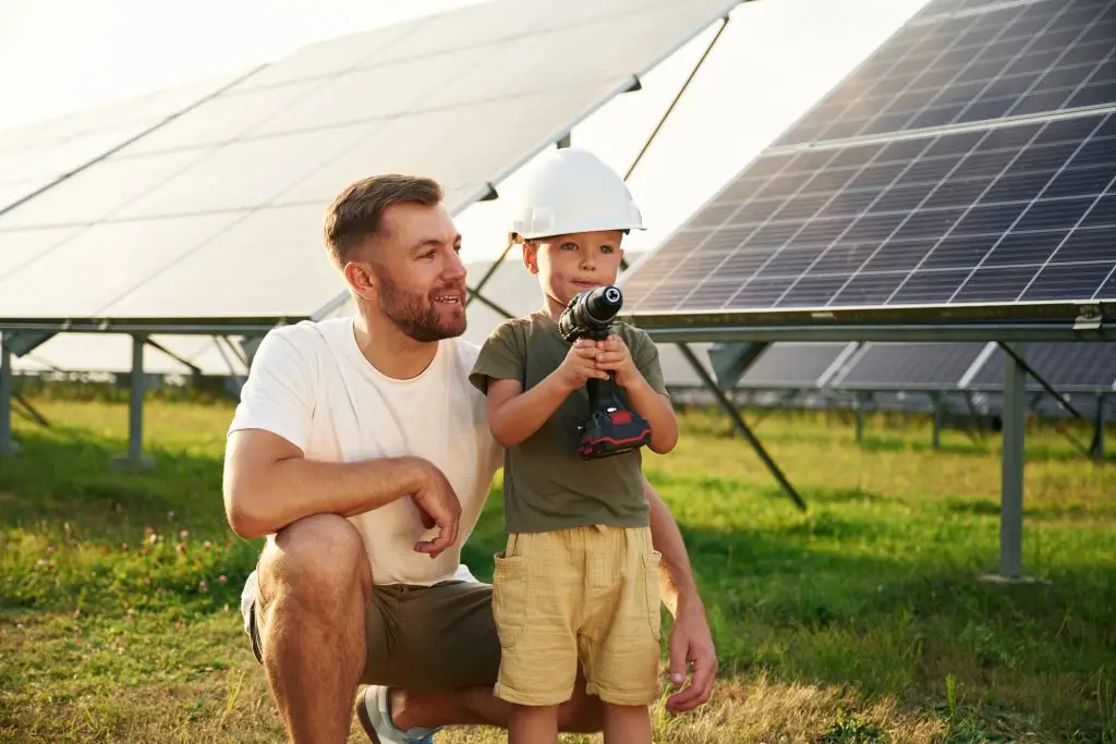 Vater und kleiner Sohn mit Bauhelm und Akkuschrauber vor einer Solaranlage.