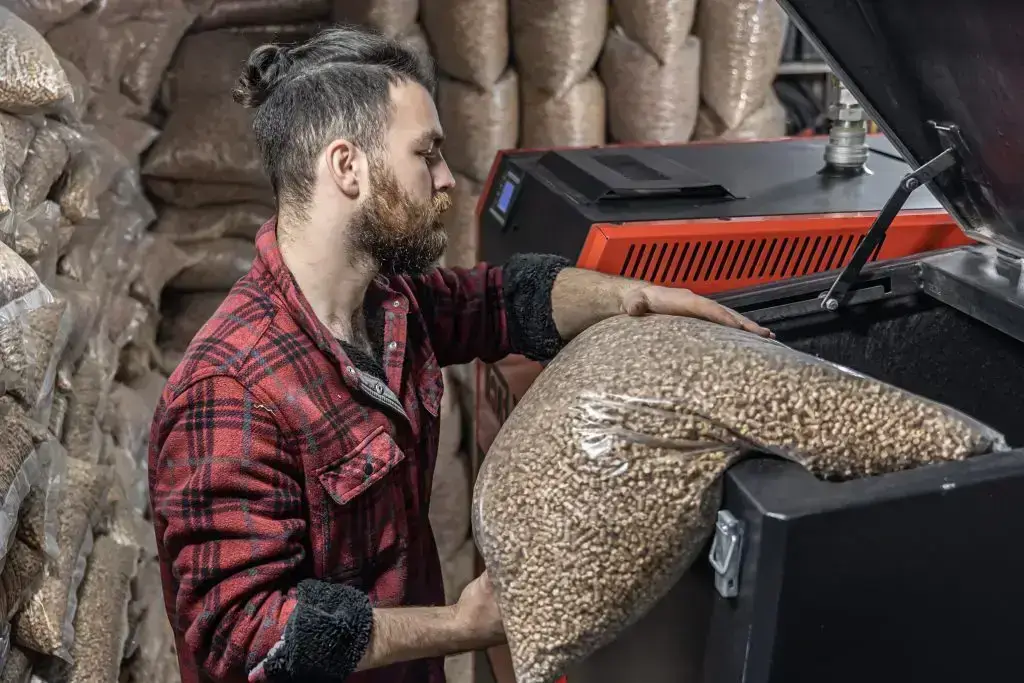 Mann lädt Pellets in einen Biomassekessel