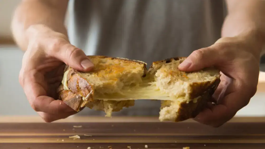 Auf dem Bild sieht man eine jungen Mann der ein gegrilltes Käsesandwich in der Hand hat