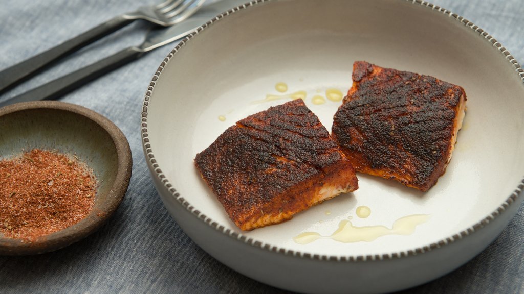 Auf dem Bild siehtt man Geschwärtzer Lachs auf einem grauen tiefen Teller angerichtet mit ein bisschen Öl über dem Lachs